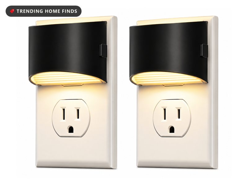 Two black and white plug-in night lights glowing warm, each with a pass-through electrical outlet below the light