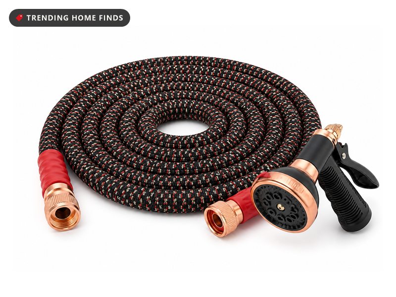Expandable garden hose in black woven braid flecked with red, coiled flat with copper couplings and a spray nozzle.