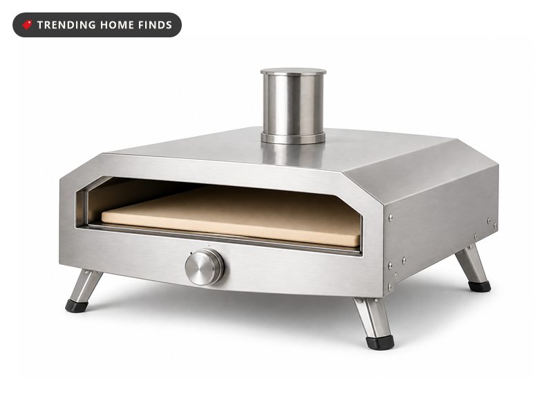 A stainless steel pizza oven glowing on a wood patio counter at night, a wooden peel sliding a pizza onto the stone floor inside.
