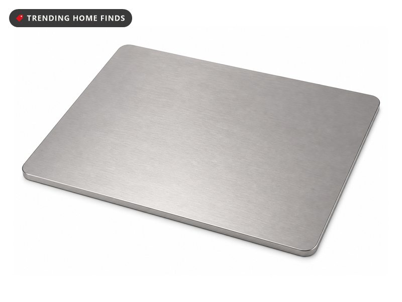 A brushed titanium chopping board on a warm oak counter before sunrise, lemon slices and a knife beside it in a non toxic kitchen.