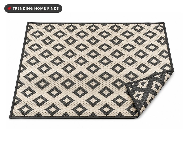 A flat woven outdoor mat in a black and cream diamond pattern with a bound black border and one corner turned back.