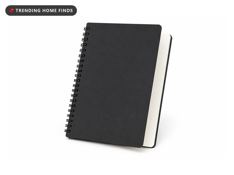 A black spiral notebook open on a bare desk in cool pre-dawn light, one dotted page being wiped clean with a grey microfiber cloth.