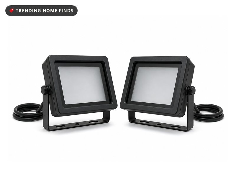 Two slim black die cast aluminum flood lights on folding brackets, their glass faces glowing violet.