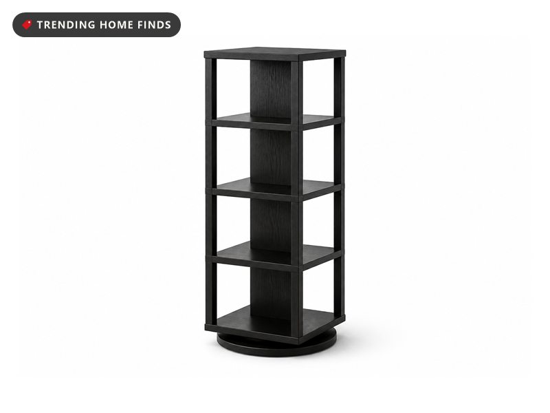 A tall five-tier black oak rotating bookshelf standing in a room corner filled with books, soft overcast daylight from a window nearby.