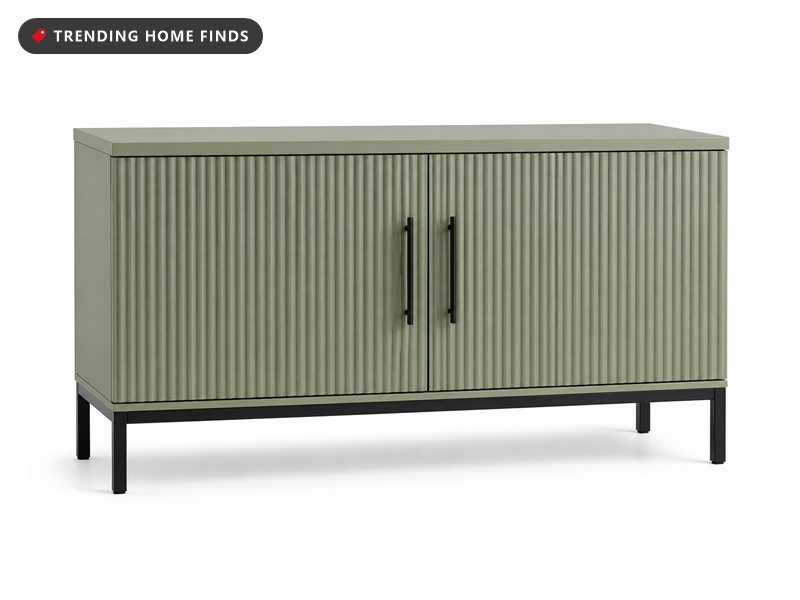 A sage green 52 inch credenza with fluted doors closed, standing under a rain-streaked window with a lamp and a ceramic vase on top.