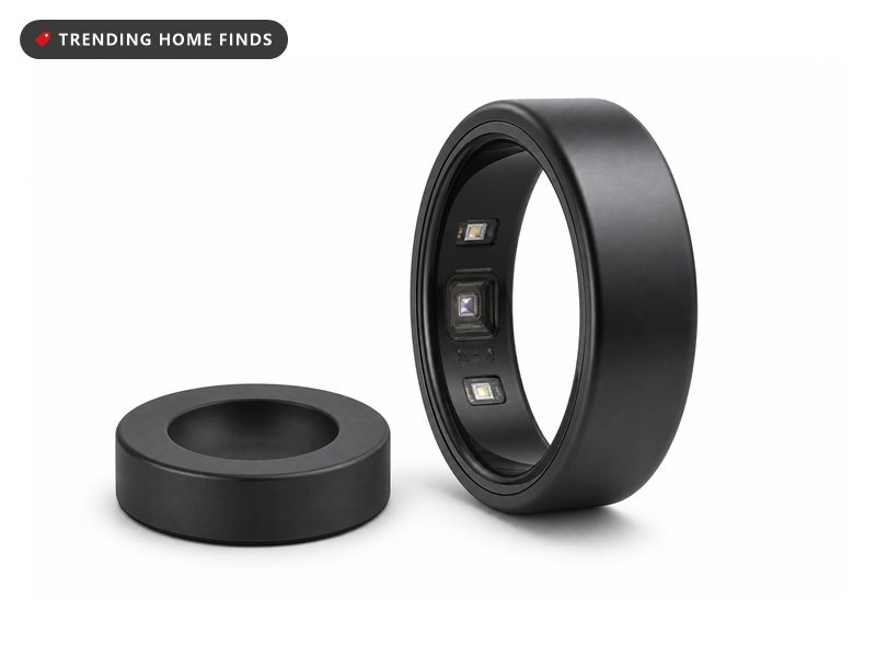A black titanium smart ring resting beside its small round charging dock on a pale marble vanity in cool pre dawn light.