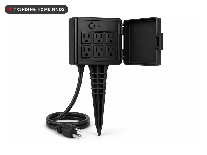 Black outdoor power stake with six grounded outlets on its face, a weatherproof cover swung open on its hinge and a cord ending in a three prong plug.