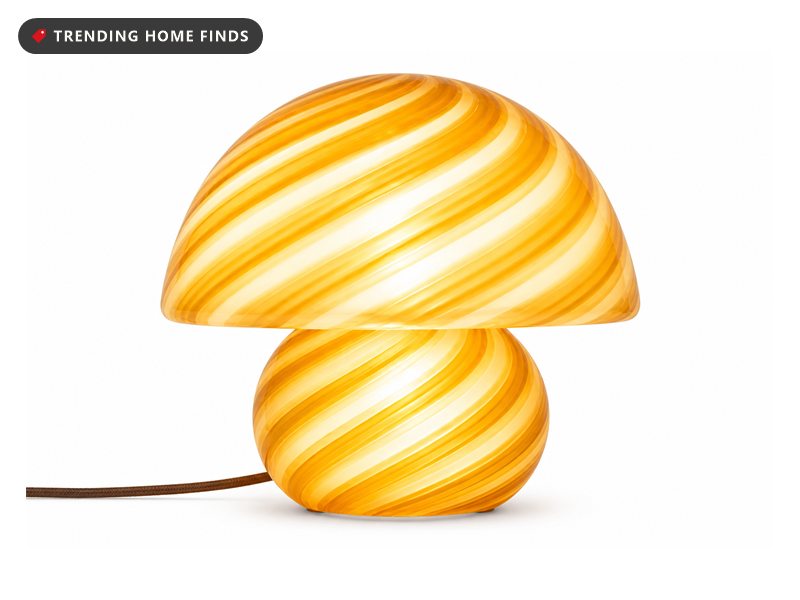 A small mushroom shaped table lamp in translucent striped glass, lit from within with a warm amber glow.