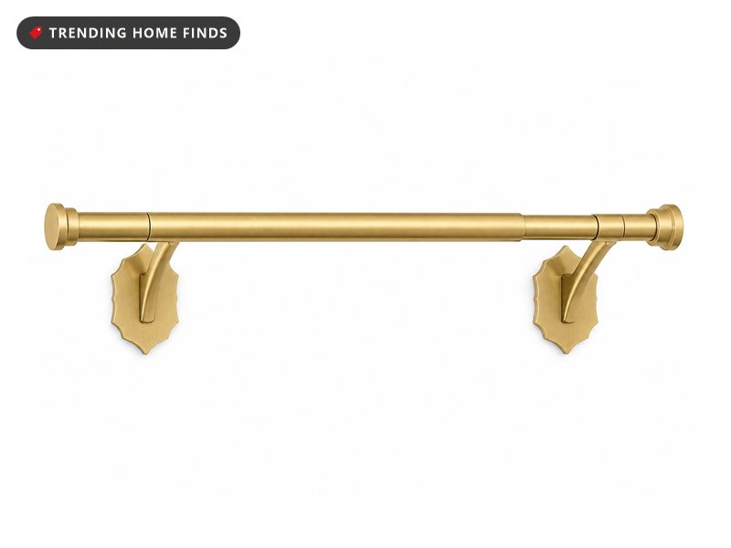Brushed gold telescoping curtain rod with flat round end caps, resting in two ornate scalloped adhesive wall brackets.