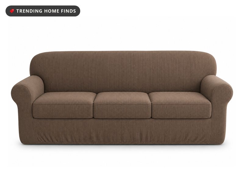 A mushroom brown ribbed chenille slipcover stretched over a three cushion sofa in a rented apartment living room, one lamp lit beside it.