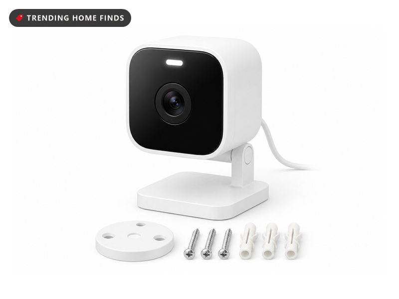 White Wyze Cam v4 security camera on a tilting base beside its teal retail box, a phone showing the live front-door feed, and mounting screws