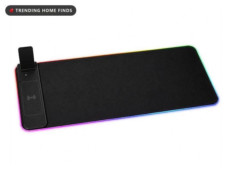 Extra long black RGB mouse pad with a glowing multicolour rim and a phone propped upright in a holder slot at the back edge